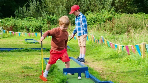 Two young boys playing crazy golf in a garden setting in summer